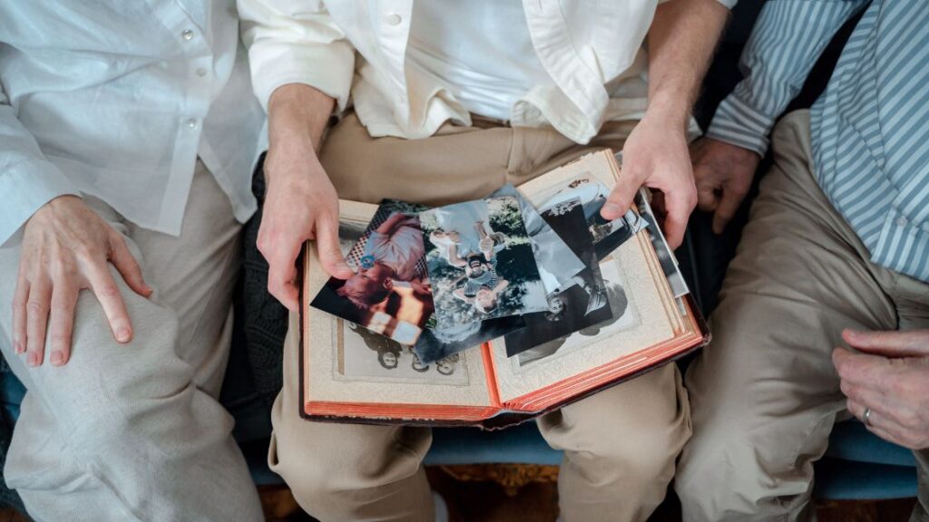 man with family history album and photos in his lap with older people sitting beside him