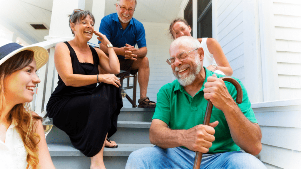 Group of intergenerational adults sitting on the steps of a house sharing a laugh.