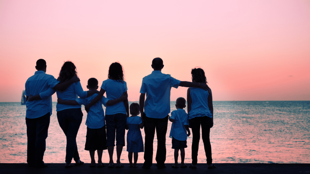 family standing arn in arm looking out over the sun setting on the ocean
