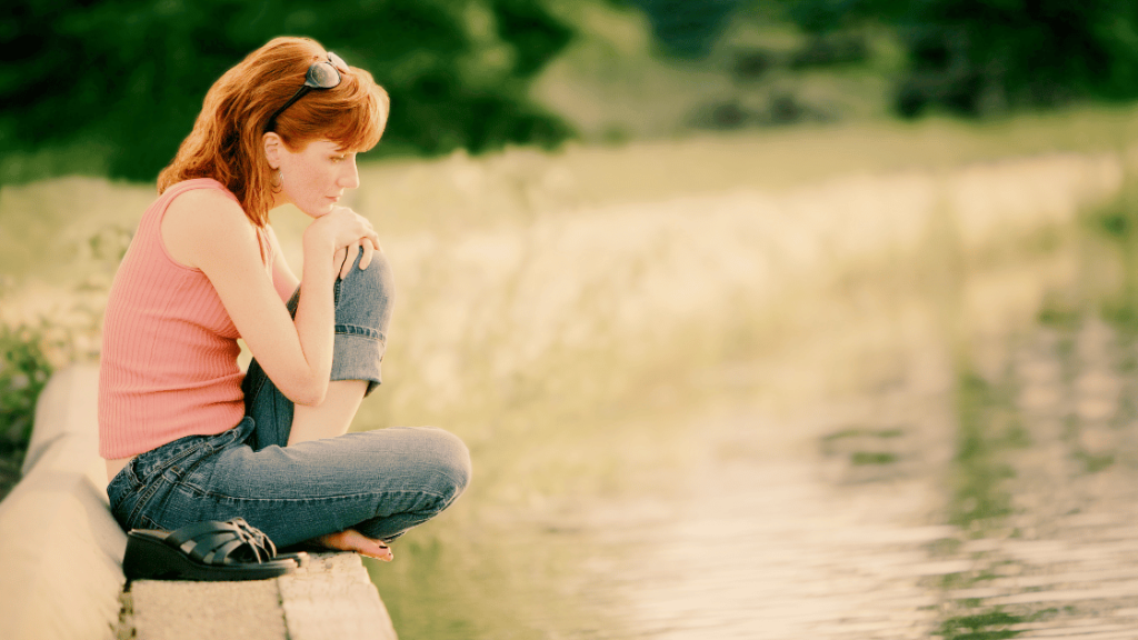 woman sitting beside a waterway looking thoughtful