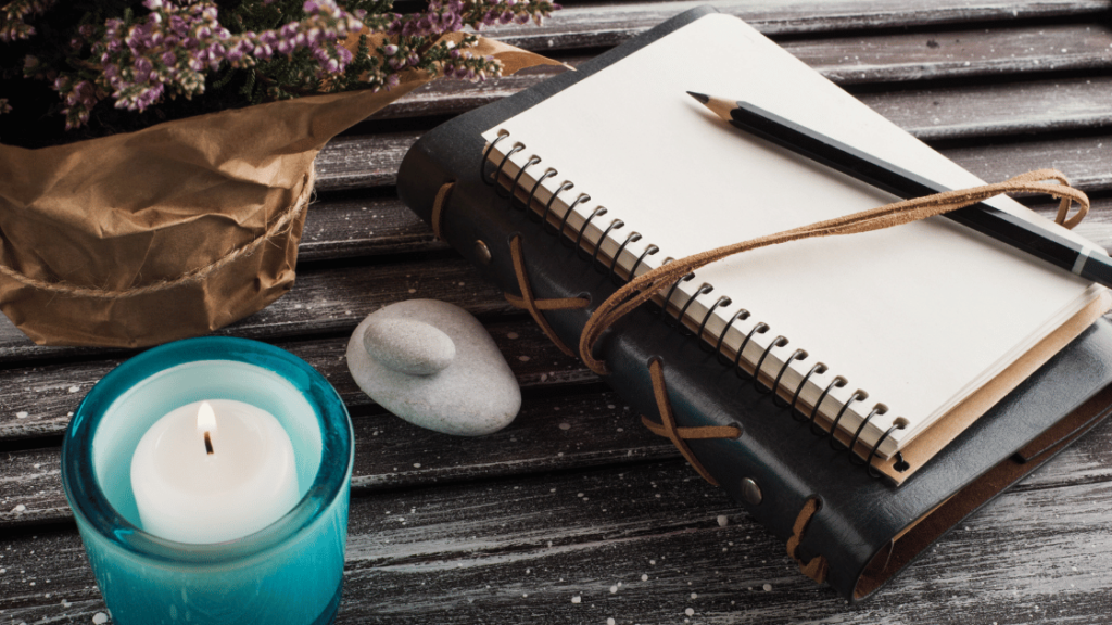 A journal, pen, and candle on a table.