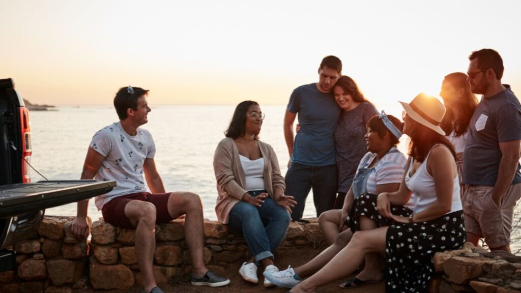 Group of people sitting beside a body of water listing to a woman telling a story.