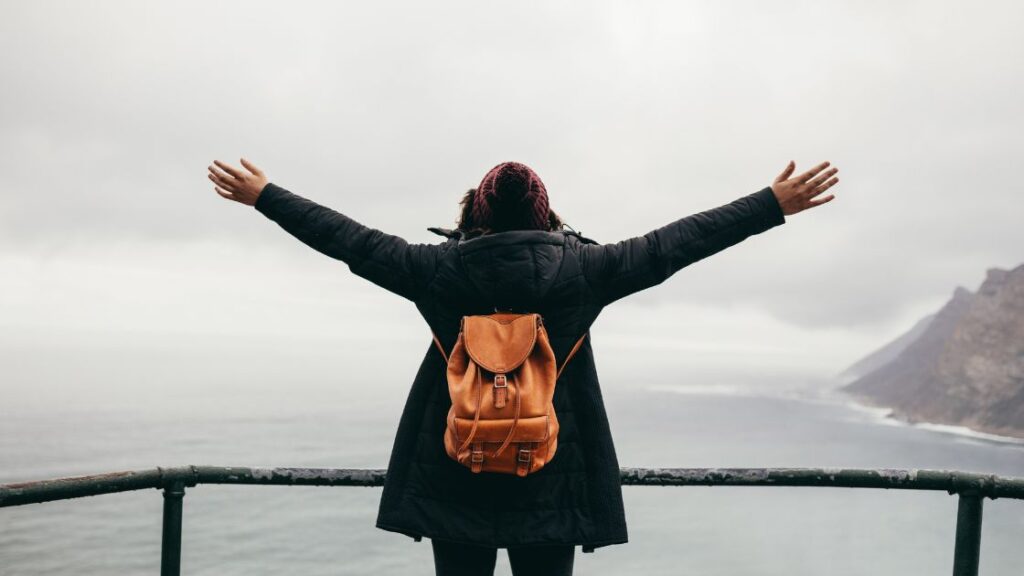 Woman with outstretch arms looking out over body of water