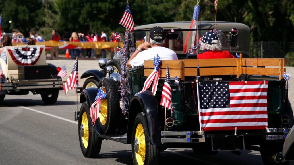 older couple driving an antique car in a traditional 4th of July parade in the United States